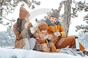 Happy family with cups of hot tea spending time together in winter forest