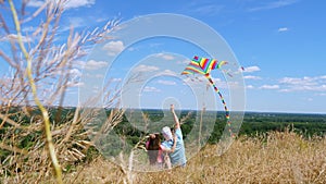 Happy family, dad and daughter, sit on cliff edge, fly a multi-colored kite, having fun, against background of amazing