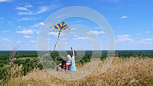 Happy family, dad and daughter, sit on cliff edge, fly a multi-colored kite, having fun, against background of amazing