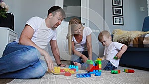 Happy family dad mom and baby 2 years playing lego in their bright living room. Slow-motion shooting happy family