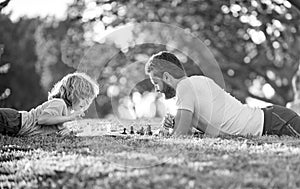 happy family of daddy and son child playing chess on green grass in park outdoor, erudite