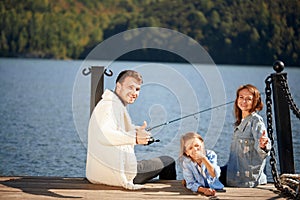 Happy family with daughter fishing in pond in fall