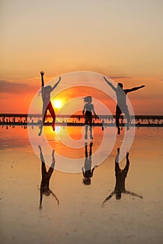 Happy family day. Silhouette of active mom, dad and little child daughter having fun jumping together on beach by