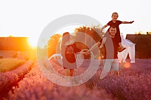 happy family day. Young mother and father carrying on shoulders daughter in lavender field on sunset. Dad, mom and child