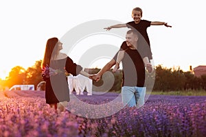 happy family day. Young mother and father carrying on shoulders daughter in lavender field on sunset. Dad, mom and child