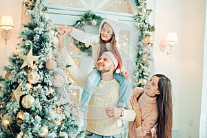 Happy family decorating a Christmas tree with boubles in the living-room