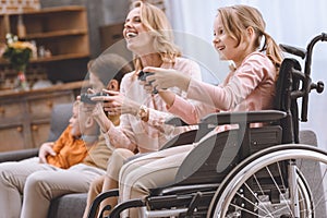 happy family with disabled child in wheelchair playing with joysticks together