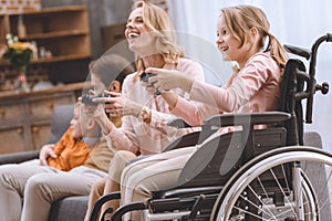 happy family with disabled child in wheelchair playing with joysticks together photo