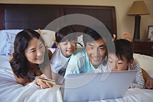 Happy family doing online shopping on laptop in the bed room