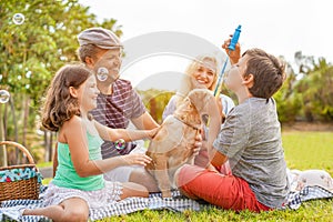 Happy family doing picnic in nature outdoor - Young parents having fun with children and their dog in summer time laughing,