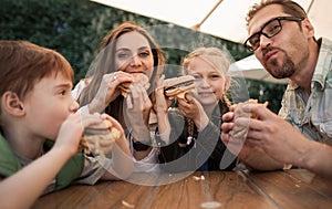 Happy family eating burgers sitting at a table in a cafe