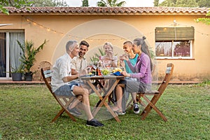 Happy family eating and drinking red wine at dinner barbecue outside. Mothers and youngsters eat together in the