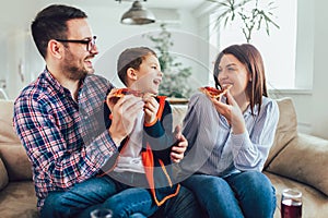 Happy family eating pizza while sitting on sofa at home