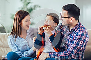 Happy family eating pizza while sitting on sofa at home