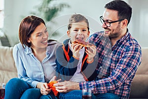 Happy family eating pizza while sitting on sofa at home