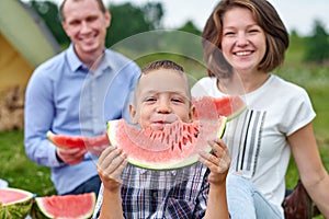 Happy family eating watermelon at picnic in meadow near the tent. Mother, father and child Enjoying Camping Holiday In Countryside