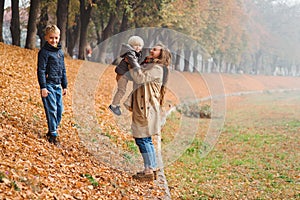 Happy family enjoing autumn day. Young mother and children on autumn walk in park. Cute brothers having fun with mom. Autumn