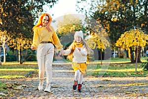 Happy family enjoying autumn weather in the park. Lovely girl with her mom having fun on the walk