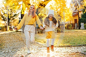 Happy family enjoying autumn weather in the park. Lovely girl with her mom having fun on the walk