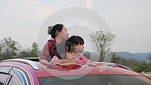 Happy family enjoying road trip on summer vacation. Mother and child enjoying nature along the way in the car on sunroof. Holiday