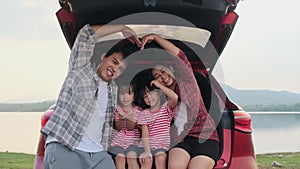 Happy family enjoying road trip on summer vacation. Mother and child sit in the trunk of the car singing along with dad playing th