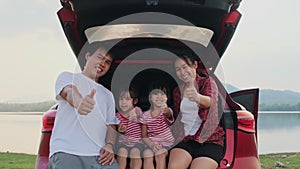 Happy family enjoying road trip on summer vacation. Mother and child sit in the trunk of the car singing along with dad playing th