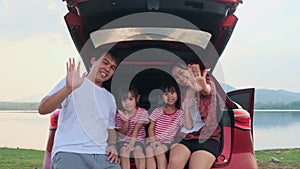 Happy family enjoying road trip on summer vacation. Mother and child sit in the trunk of the car singing along with dad playing th