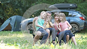 Happy family enjoying time at capmsite outdoors. Parents and their children sitting together and talking happily.