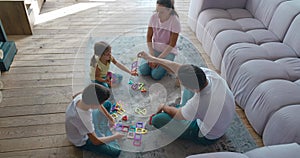 Happy family enjoying time with children playing magnetic constructor sitting on sofa floor. A middle-aged father helps