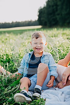 Happy family enjoying together in summer day. Little boy sitting on grass