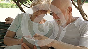 Happy family enjoying vacation in Europe. Seniors sitting on bench in park browsing in smartphone