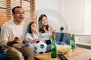 A happy family enjoys the thrill of a football match at home