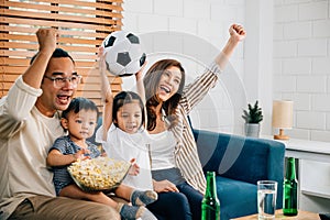 A happy family enjoys the thrill of a football match at home