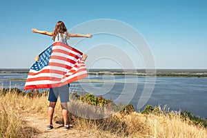 Happy family father with America flag and daughter sitting on fathers shoulders enjoy nature. View from the back