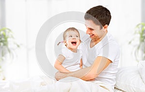 Happy family father and baby daughter playing in bed