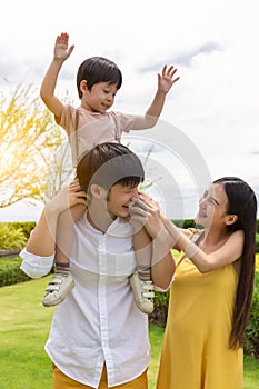 Happy family. Father carry cute son on shoulder, playing at park, mother look at son with love and husband looks at wife with love