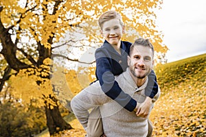 Happy family father and child boy in the autumn leaf fall in park holding his child on his back