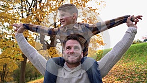 Happy family father and child boy on his shoulder in the autumn leaf fall in park