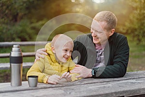 Happy Family: Father And Child Boy Son Playing And Laughing In Autumn Park, Sitting On Wooden Bench And Table. Father