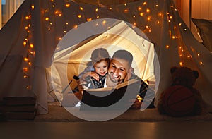 Happy family father and child daughter reading a book in tent