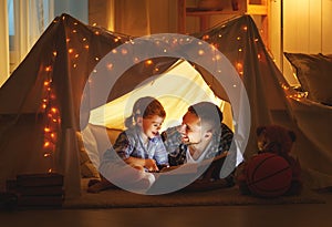 Happy family father and child daughter reading a book in tent