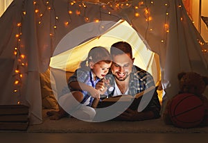 Happy family father and child daughter reading a book in tent photo