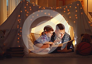 Happy family father and child daughter reading a book in tent