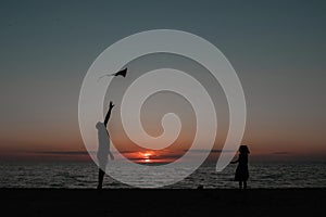 happy family father and child daughter run with kite in the meadow. silhouettes on the background of the sea sunset.