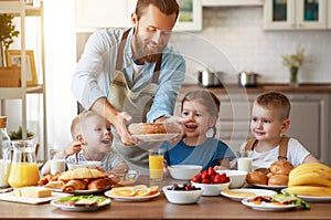 Happy family father with children feeds his sons and daughter in kitchen with Breakfast