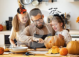 Happy family   father and children prepare for Halloween by carving pumpkins at home in kitchen