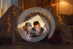 Happy family father and children reading a book in tent at hom