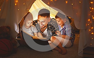 Happy family father and children reading a book in tent at hom