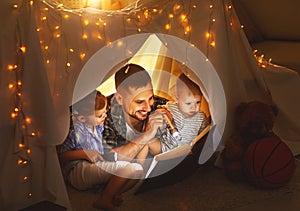 Happy family father and children reading a book in tent at hom