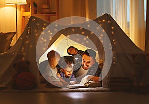 Happy family father and children reading a book in tent at hom